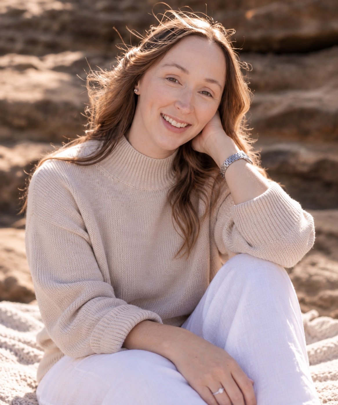 Caitlin sitting on the beach in a cream jumper